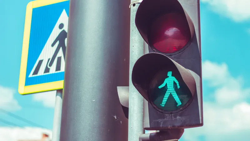 Pedestrian traffic light with green color on a black metallic bar near a crosswalk traffic sign