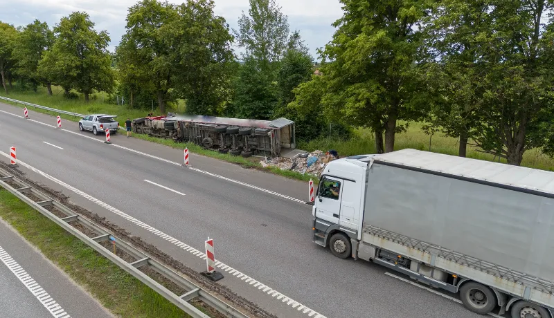 An aerial view of a truck accident scene on a highway. A red truck is off the road, with debris scattered nearby.
