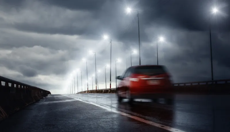 Blurry of car driving fast on bridge during hard rain with storm clouds as background