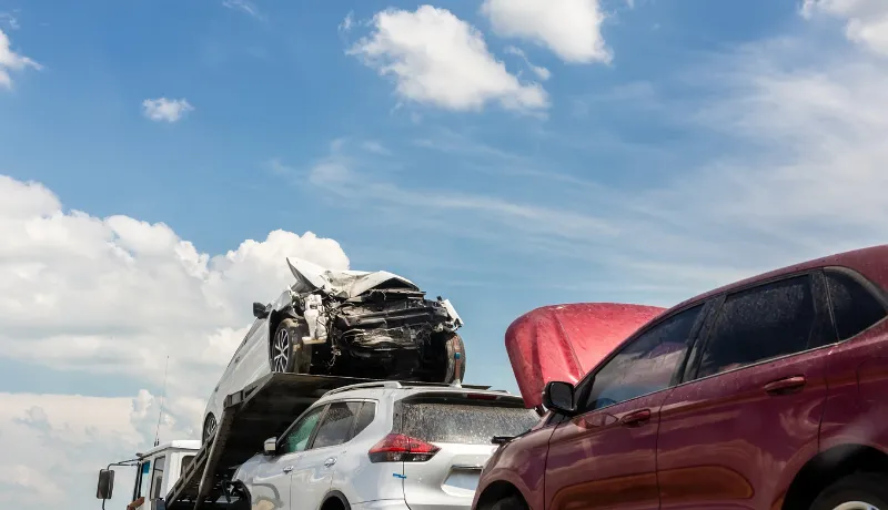 Tow truck trailer on highway carrying three damaged cars sold on insurance car auctions for repair and recovery.