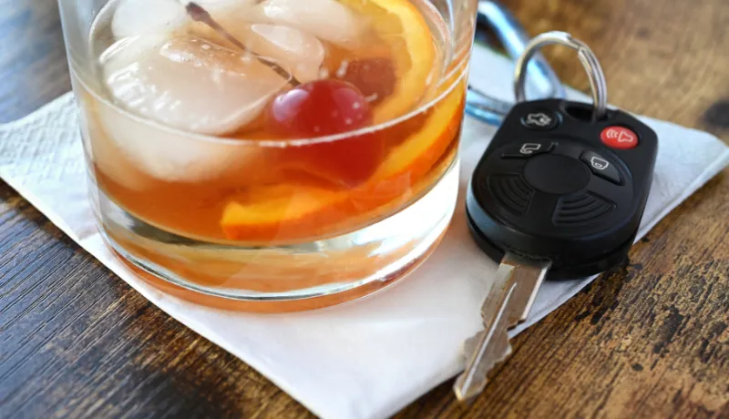Drink and Drive, drunk driver concept - mixed drink liquor cocktail with key for vehicle at bar