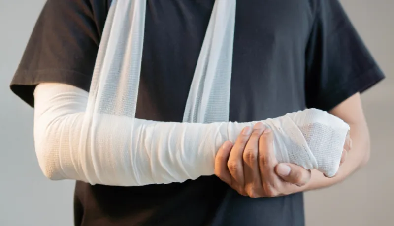 Close-up of man with bandaged hand and arm support standing over light gray color background.