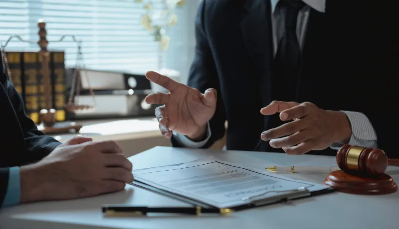 Lawyer gesturing with hands while discussing contract details with client in office, surrounded by legal documents and a gavel resting on the desk