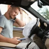 A man holding his phone while his other hand is placed on the back of his neck.