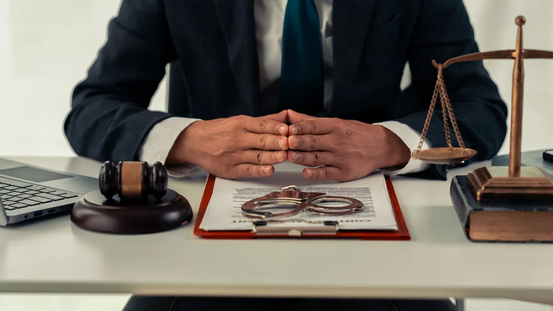 Lawyer in suit signing legal document at table with justice scale, close-up
