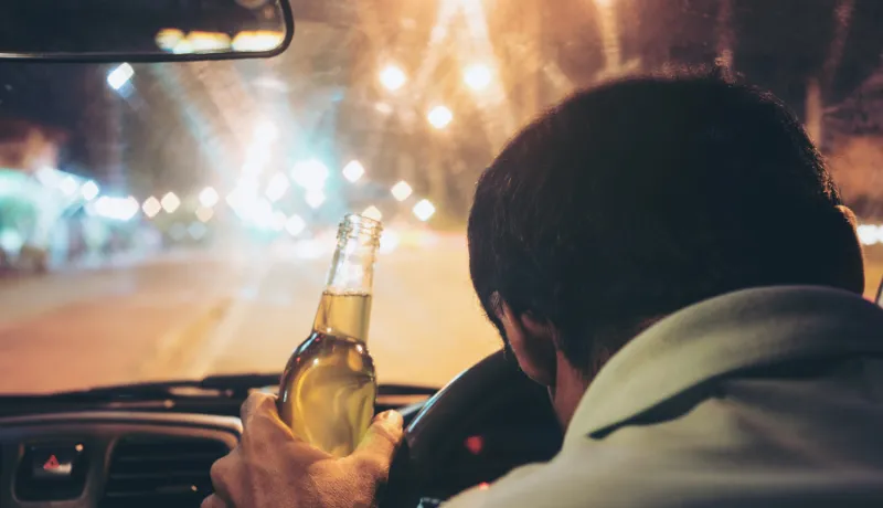 Drunk young man drives a car with a bottle of beer. This is a campaign picture of "Don't Drink for Drive