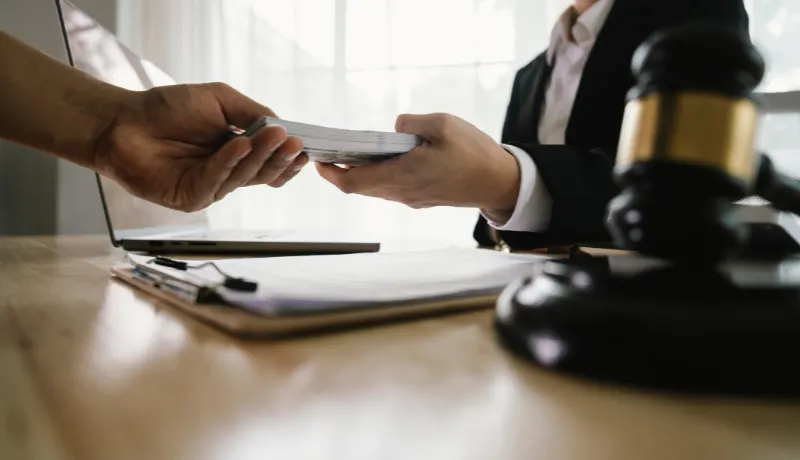A hand holding stacks of money is shown being exchanged with another hand, implying a transaction, payment