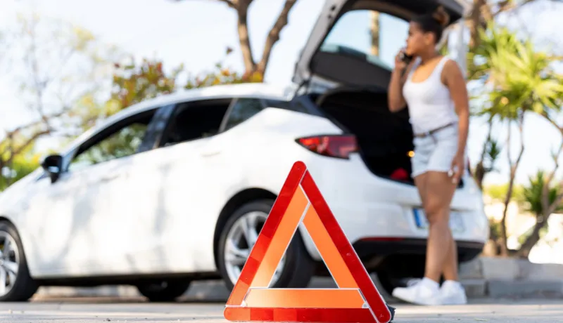 road signaling car breakdown or accident with female driver using phone in background calling for help