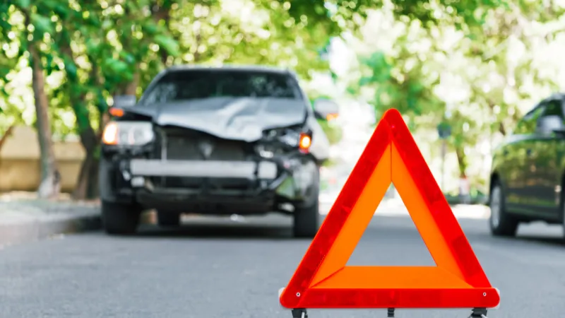 Red emergency stop triangle sign on road during a car accident. Broken gray car in road traffic accident.