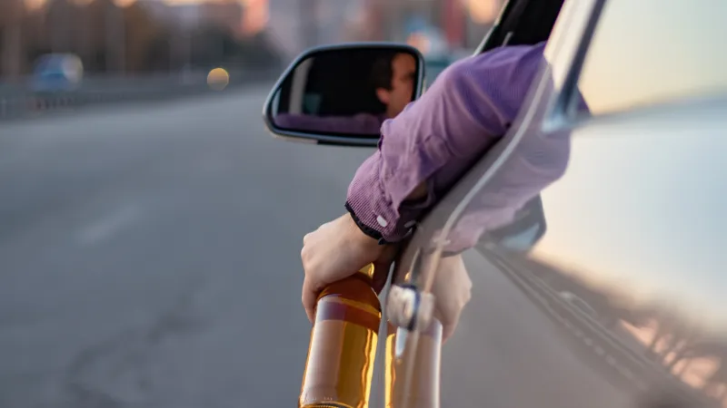 concept of alcohol, dangerous driving. drink and drive. man drinks off a bottle of beer while driving car.