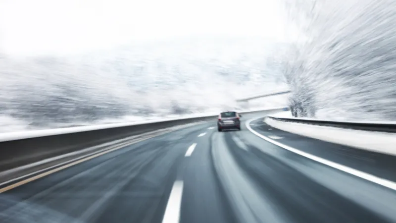 Blurry fast turn at the icy snow road with one car in the foreground.