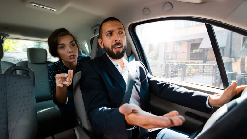 Taxi driver driving a car and having an argument with female passenger.