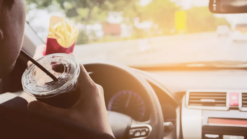 Man driving car while eating French fries and soft drink