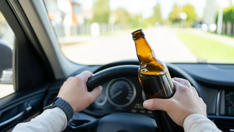 A drunken man driving a car with a bottle of alcohol in his hand.