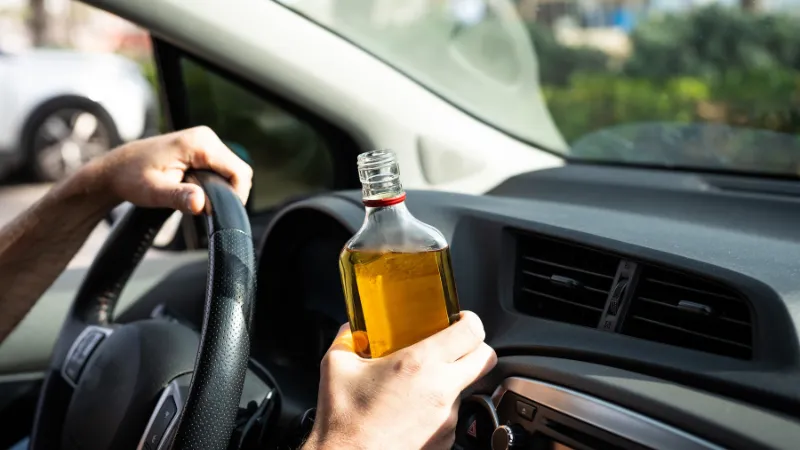 Man holding a bottle of alcohol while driving a car,