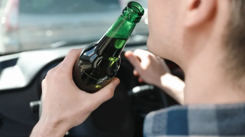 A man driving while drinking an alcoholic beverage