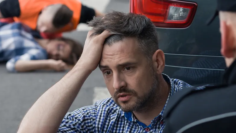 A confused man who could not speak because of the accident, with an unconscious woman and a rescuer lying behind him.