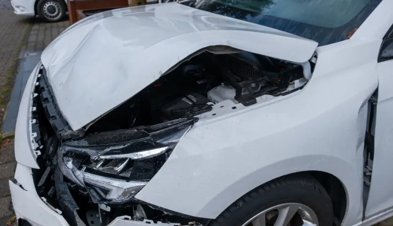 front of white crashed car close up, badly damaged car after car accident, huge dent in car body, reckless driving