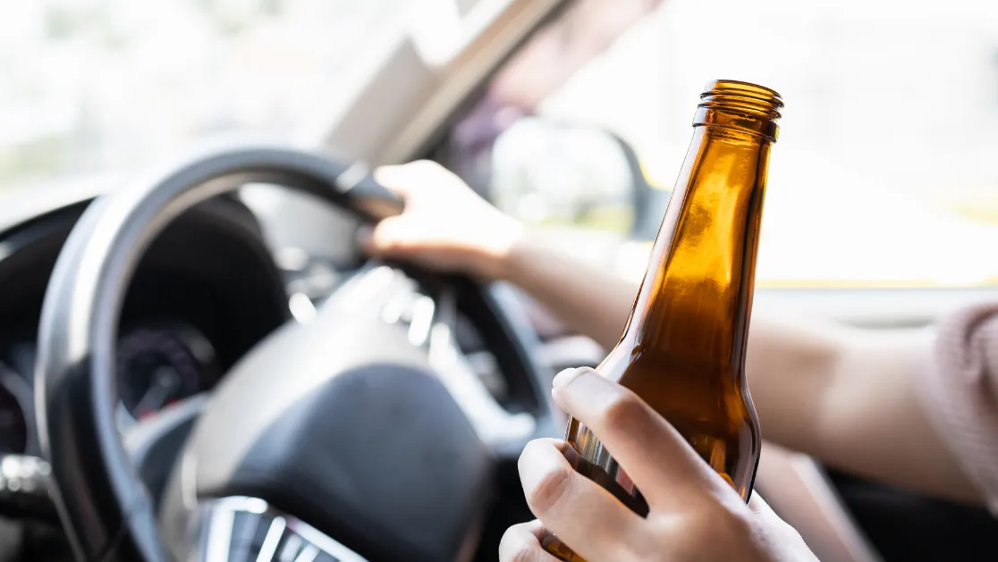Idriver holding bottle of beer, drinking alcohol while driving motor vehicle