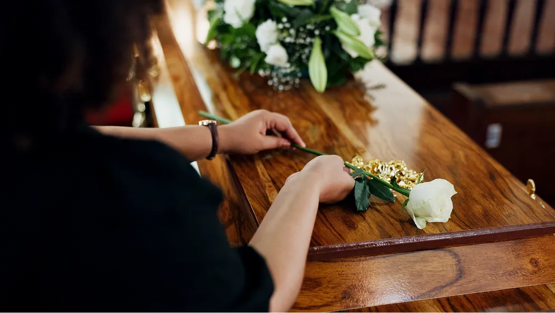A woman holding a white rose placed in a casket at the funeral.